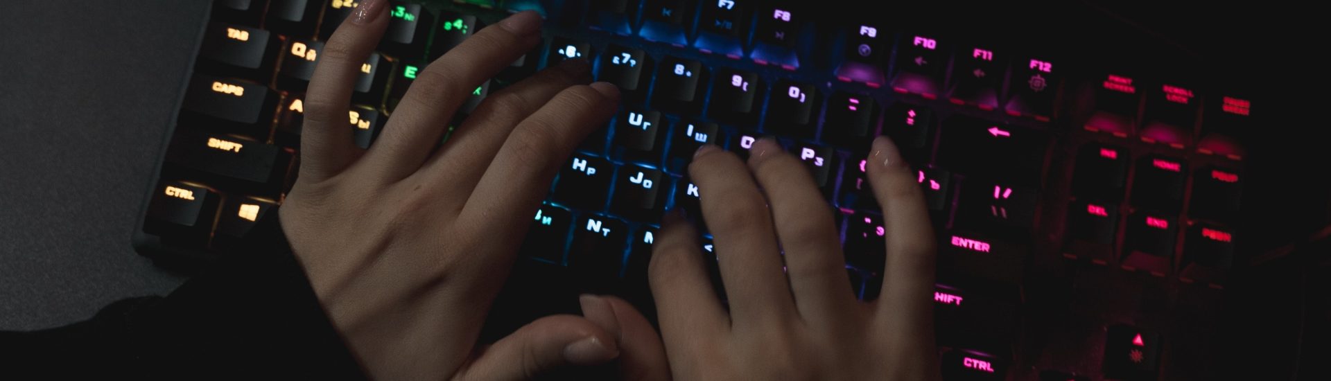 Hände, die auf bunt leuchtende Tastatur tippen