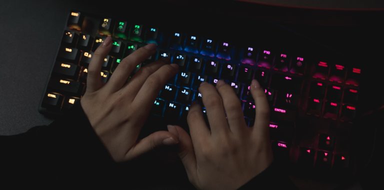 Hände, die auf bunt leuchtende Tastatur tippen